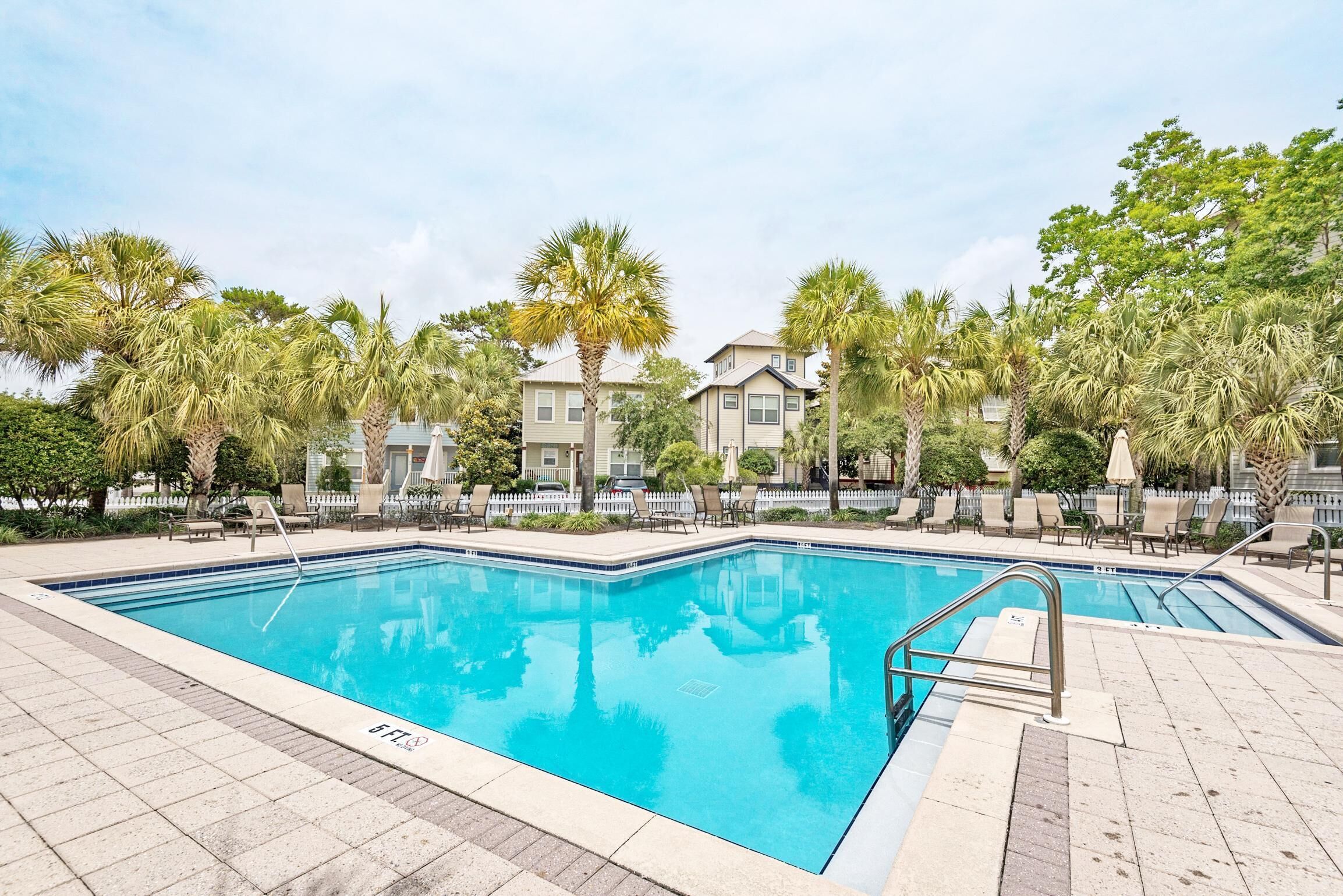 A rectangular swimming pool with a tiled deck, surrounded by palm trees and lounge chairs.
