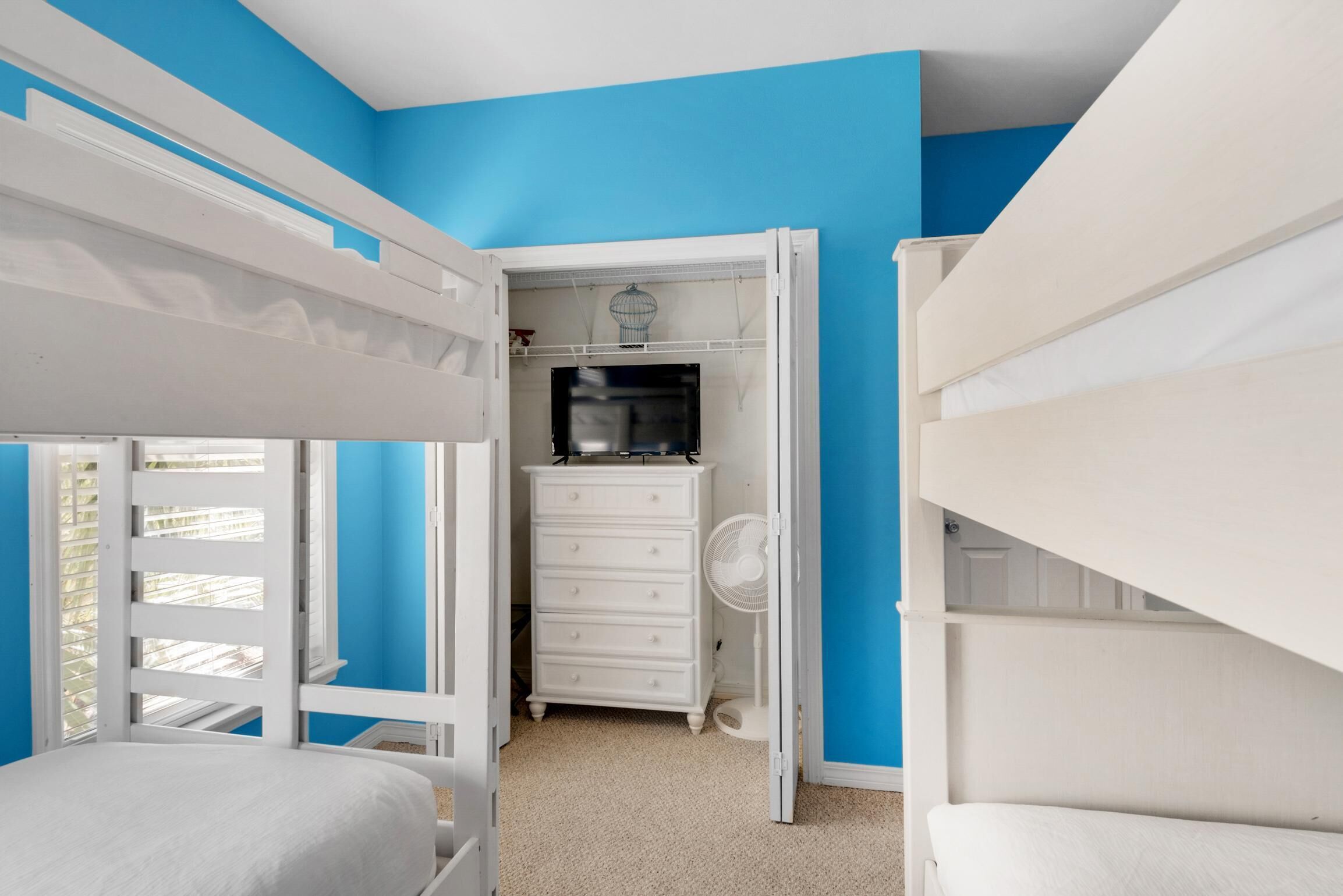 Une chambre avec des lits superposés, une commode et un placard équipé d’un ventilateur.