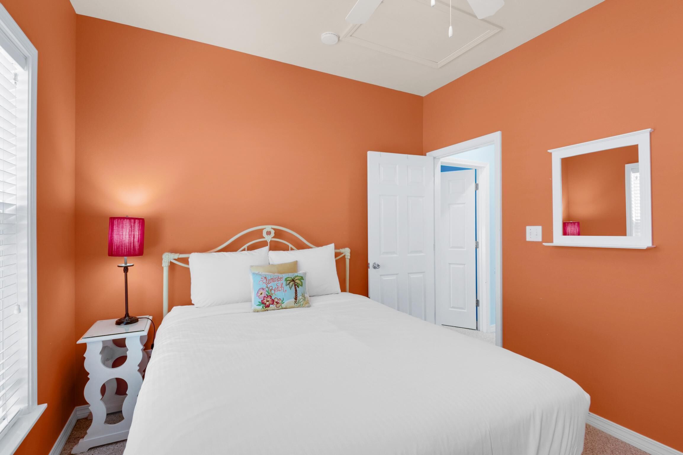 Une chambre avec un mur orange, un lit blanc et une table de chevet avec une lampe.