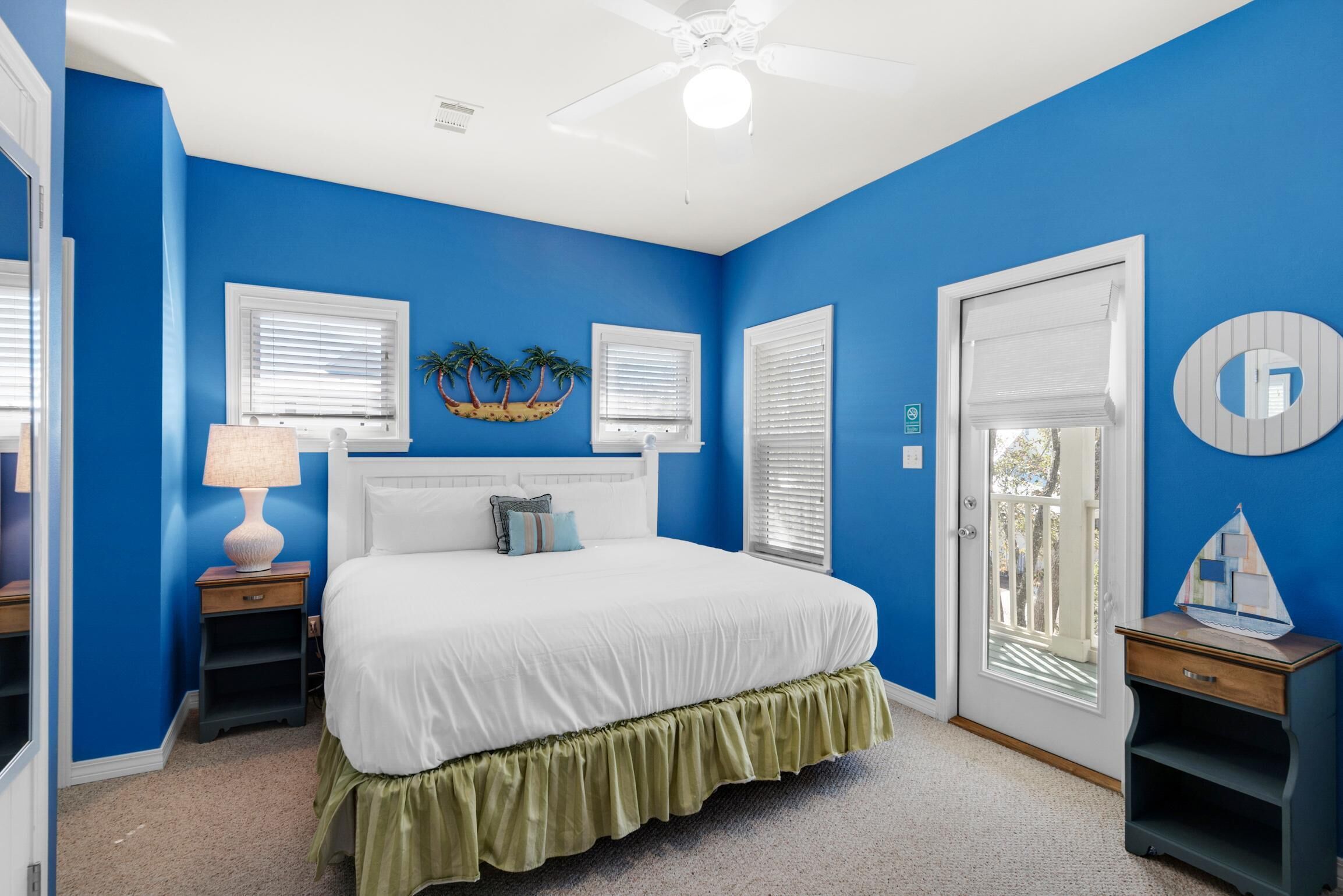 Ein Schlafzimmer mit einem weißen Bett, blauen Wänden und einem weißen Deckenventilator.