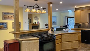 A modern kitchen with a central island, wooden cabinets, a black stove, and a tiled backsplash. - Relax and Rejuvinate at the cottage.  Get some forest therapy. (Bridgenorth)