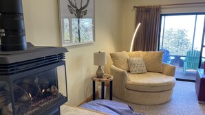 A cozy living room with a fireplace, a comfortable sofa, a small table with a lamp, and a window with curtains. - Relax and Rejuvinate at the cottage.  Get some forest therapy. (Bridgenorth)