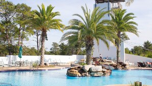 A pool area with lounge chairs, palm trees, and a rock feature. - Chalet Mer (Santa Rosa Beach)