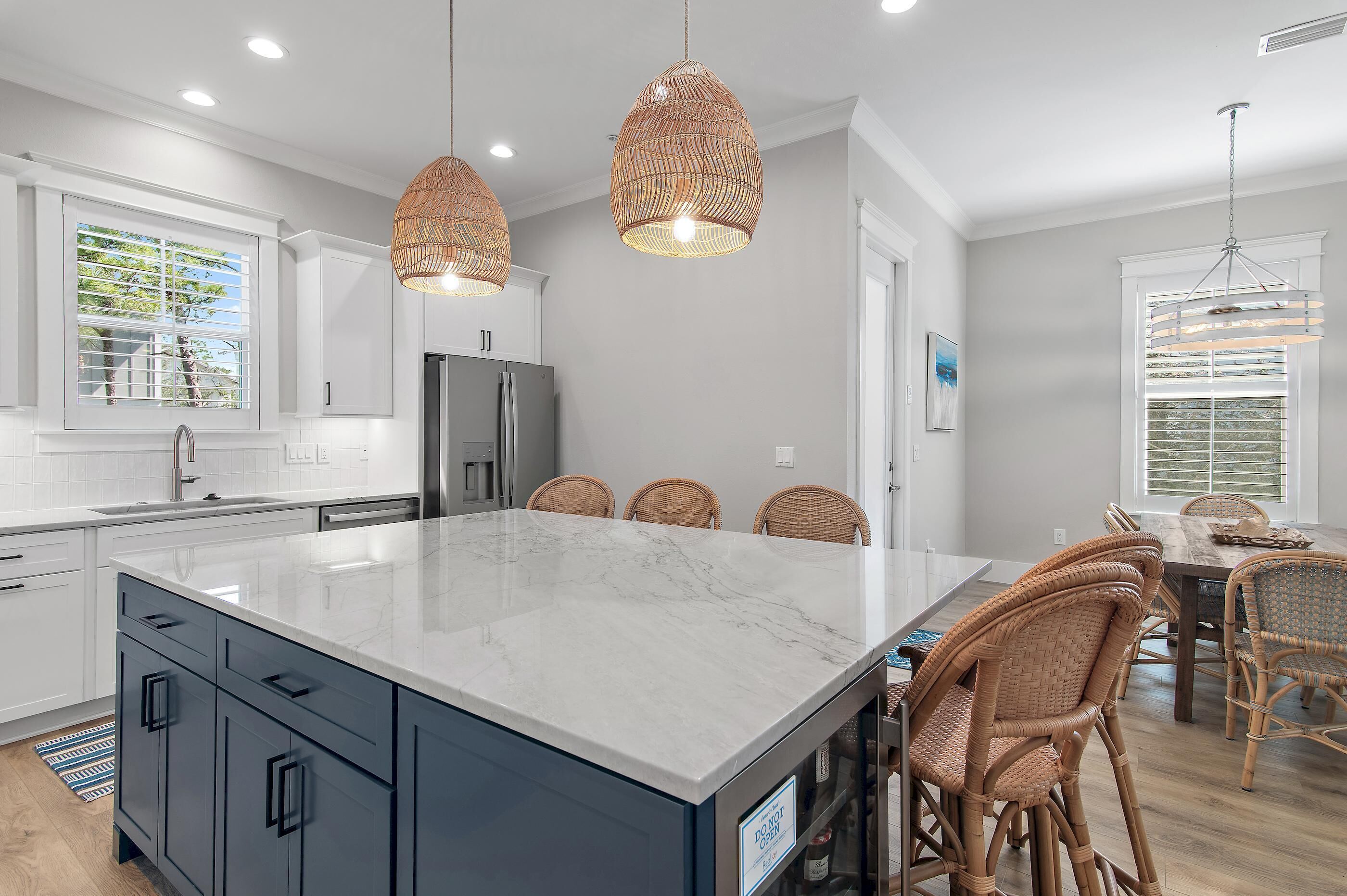 A modern kitchen with a large island, white cabinetry, and wicker pendant lights.