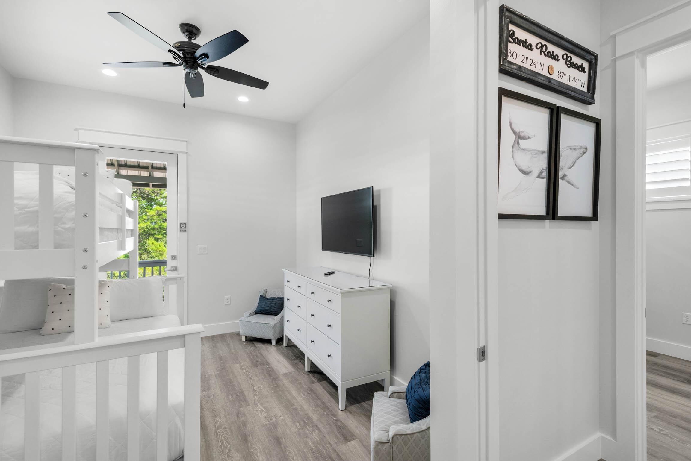 A bedroom with a bed, a dresser, a TV, and a ceiling fan.