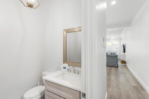 A modern bathroom with a white sink, a mirror, and a toilet. - Blue Heron Hideaway (Santa Rosa Beach)
