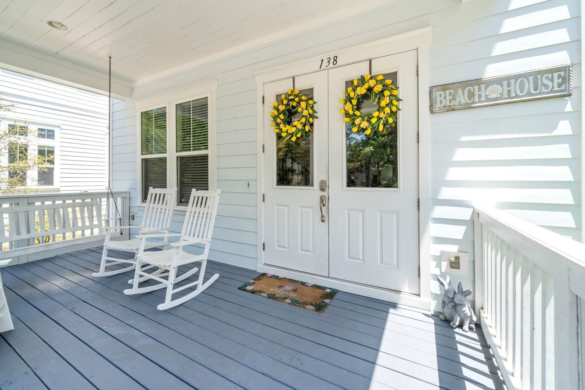 Eine Veranda mit weißen Schaukelstühlen, einer Tür mit einem Kranz und einem Schild mit der Aufschrift 'Beach House'.