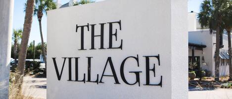 A sign reading "THE VILLAGE" with palm trees and a building in the background.
