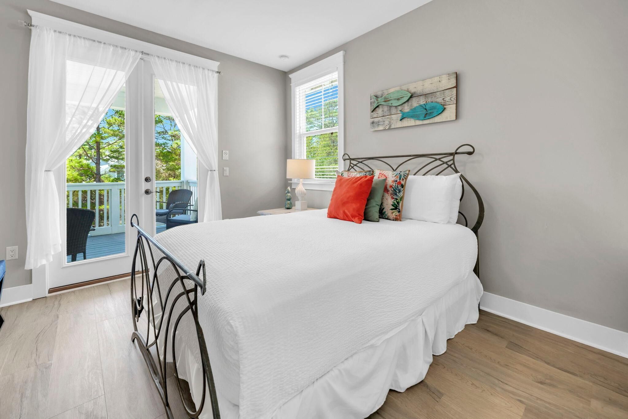 A bedroom with a bed, a window with curtains, a chair, and a wall with a fish painting.