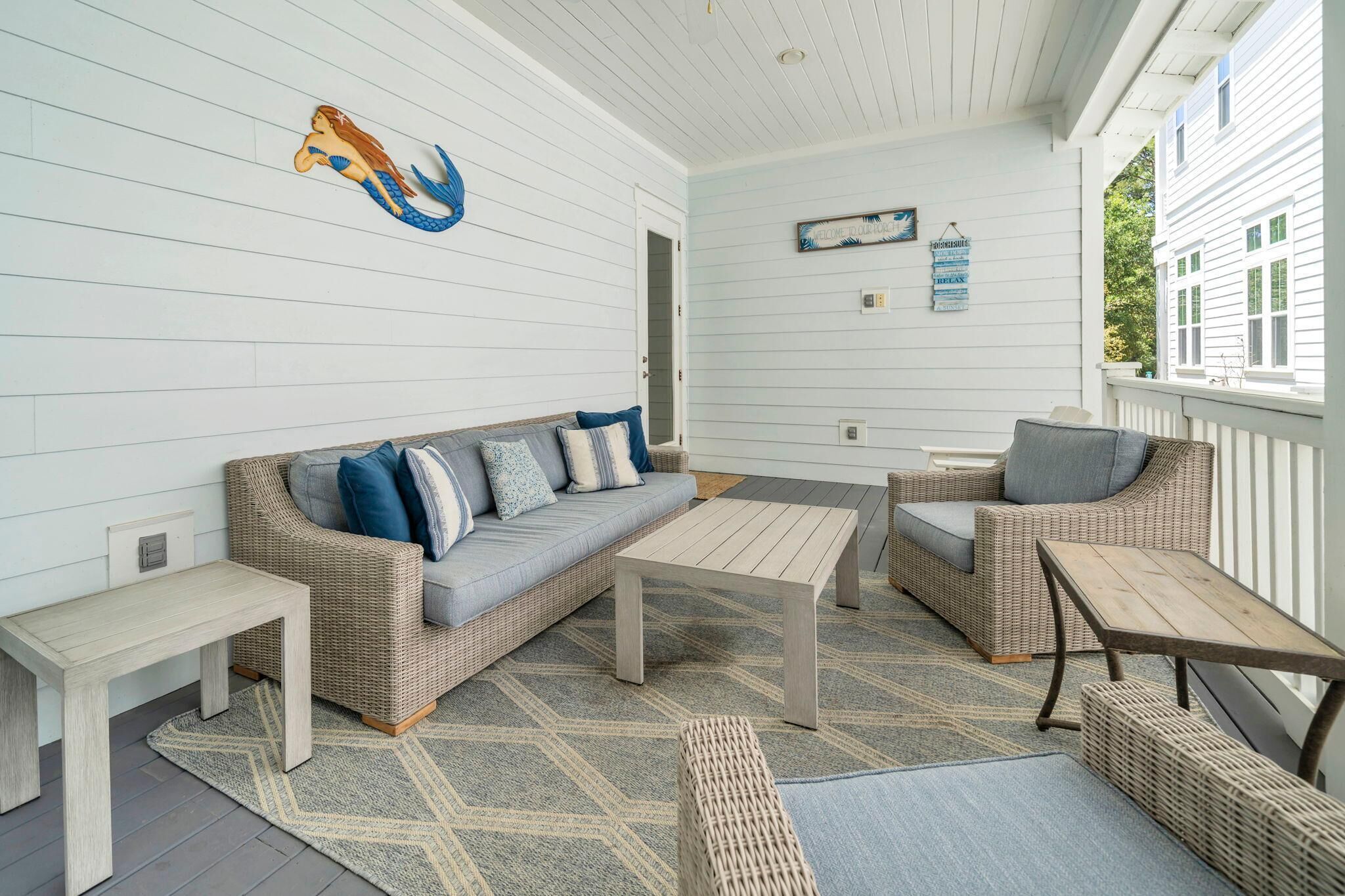 A covered porch with a sofa, two chairs, a coffee table, and a bench.