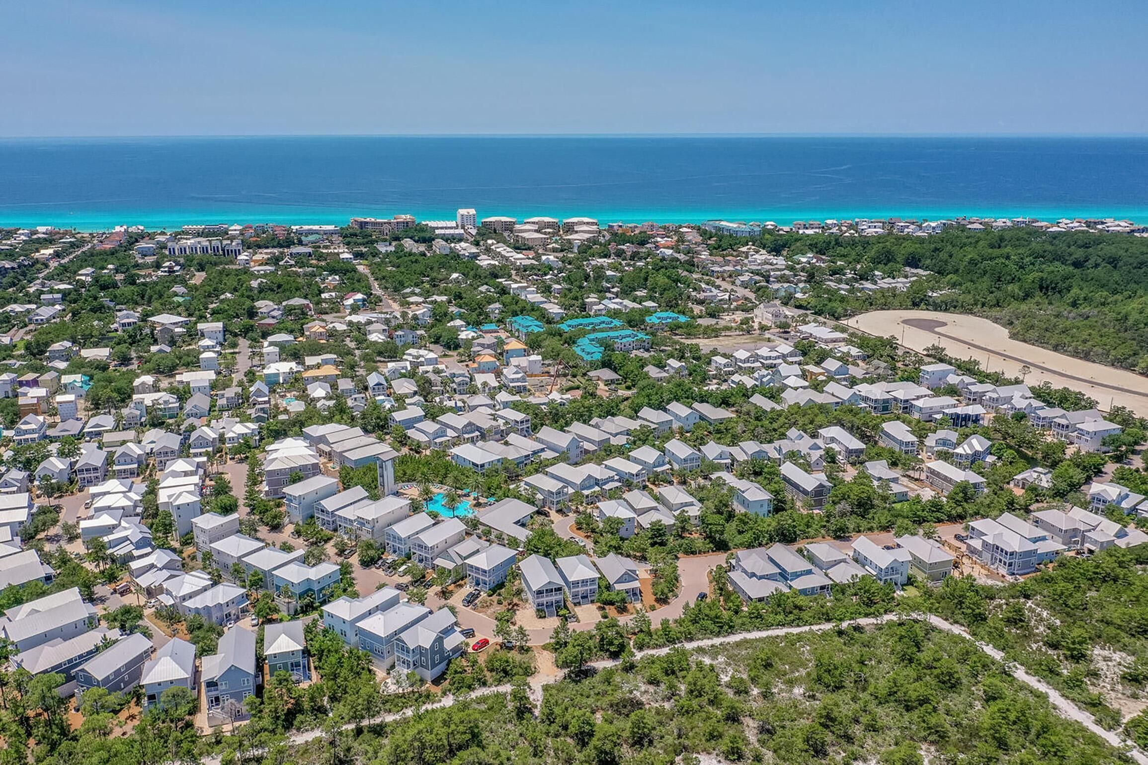 An aerial view of a coastal residential area with houses, a beach, and a clear view of the ocean.