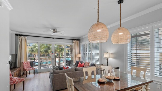 A spacious living room with a grey sofa, red patterned chairs, a wooden dining table, and large windows with blinds. - Adagio F205 (Santa Rosa Beach)