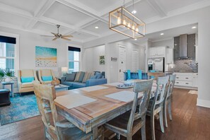 A spacious living area with a wooden dining table, blue chairs, a sofa, and a ceiling fan. - 30A Sunshine Shack (Santa Rosa Beach)