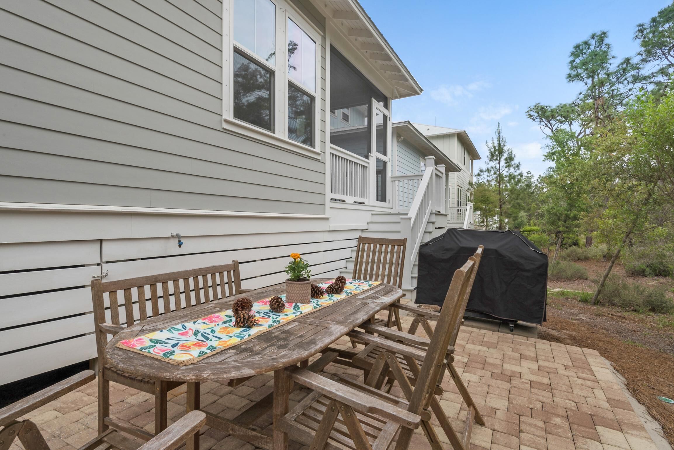 A wooden table with chairs and a bench, a covered grill, and a house with white siding and a porch.