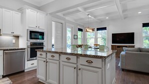 A modern kitchen with white cabinetry, a built-in oven, and a large island with a glass top. - 30A Sunshine Shack (Santa Rosa Beach)