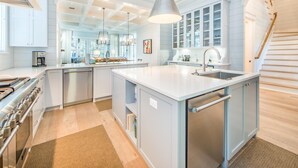 Een moderne keuken met een centraal eiland, roestvrijstalen apparatuur en een grote hanglamp.