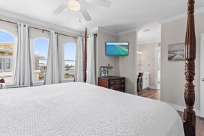 Een slaapkamer met een groot bed, een plafondventilator, een televisie en uitzicht op het strand.