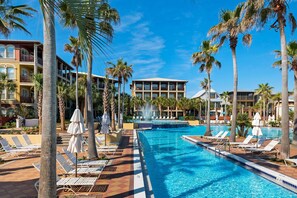 Ein Poolbereich eines Resorts mit Liegestühlen, Palmen und blauem Himmel.