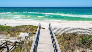 Ein hölzerner Steg führt zu einem Strand mit Blick auf das Meer.