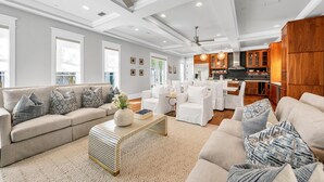A spacious living room with a large sofa, a coffee table, and a kitchen area in the background. - The Atticus (Panama City Beach)