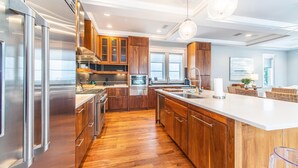 A modern kitchen with wooden cabinets, stainless steel appliances, and a large island. - The Atticus (Panama City Beach)