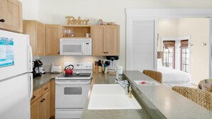 A compact kitchen with wooden cabinets, a white refrigerator, a microwave, a stove, and a sink. - Sunsets at Rosemary Carriage House (Panama City Beach)