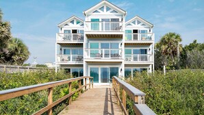 A multi-story beachfront building with balconies, a wooden boardwalk leading to the entrance, and lush greenery surrounding the property. - Ramsgate 3 (Panama City Beach)