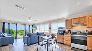 A modern kitchen with wooden cabinets, a stove, and a dining area with a table and chairs. - Ramsgate 3 (Panama City Beach)