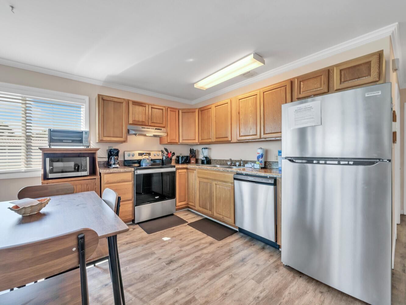 A modern kitchen with wooden cabinets, stainless steel appliances, a dining table, and a built-in oven.