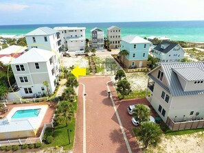 Una zona residenziale costiera con diverse case a due piani, un vialetto lastricato e una piscina.