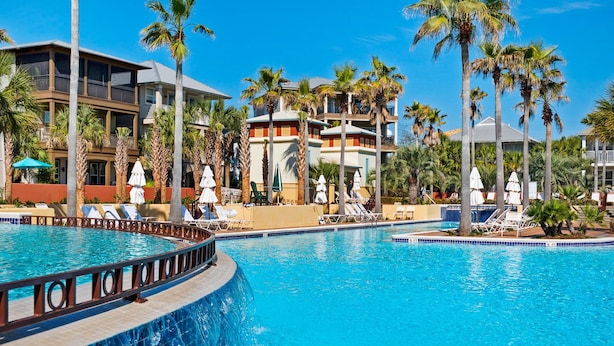 Un resort con una gran piscina, palmeras y edificios de varios pisos con balcones.