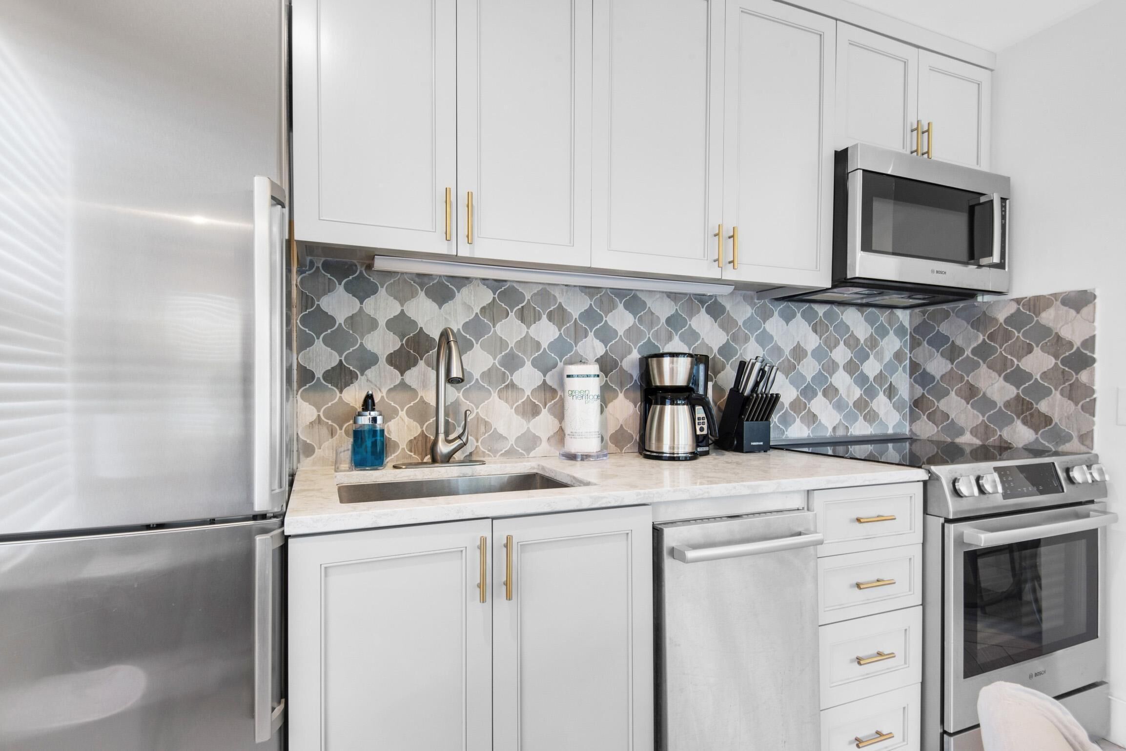 Una cocina moderna con armarios blancos, un refrigerador de acero inoxidable, un microondas, una cafetera y una estufa.