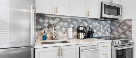 Una cocina moderna con armarios blancos, un refrigerador de acero inoxidable, un microondas, una cafetera y una estufa.
