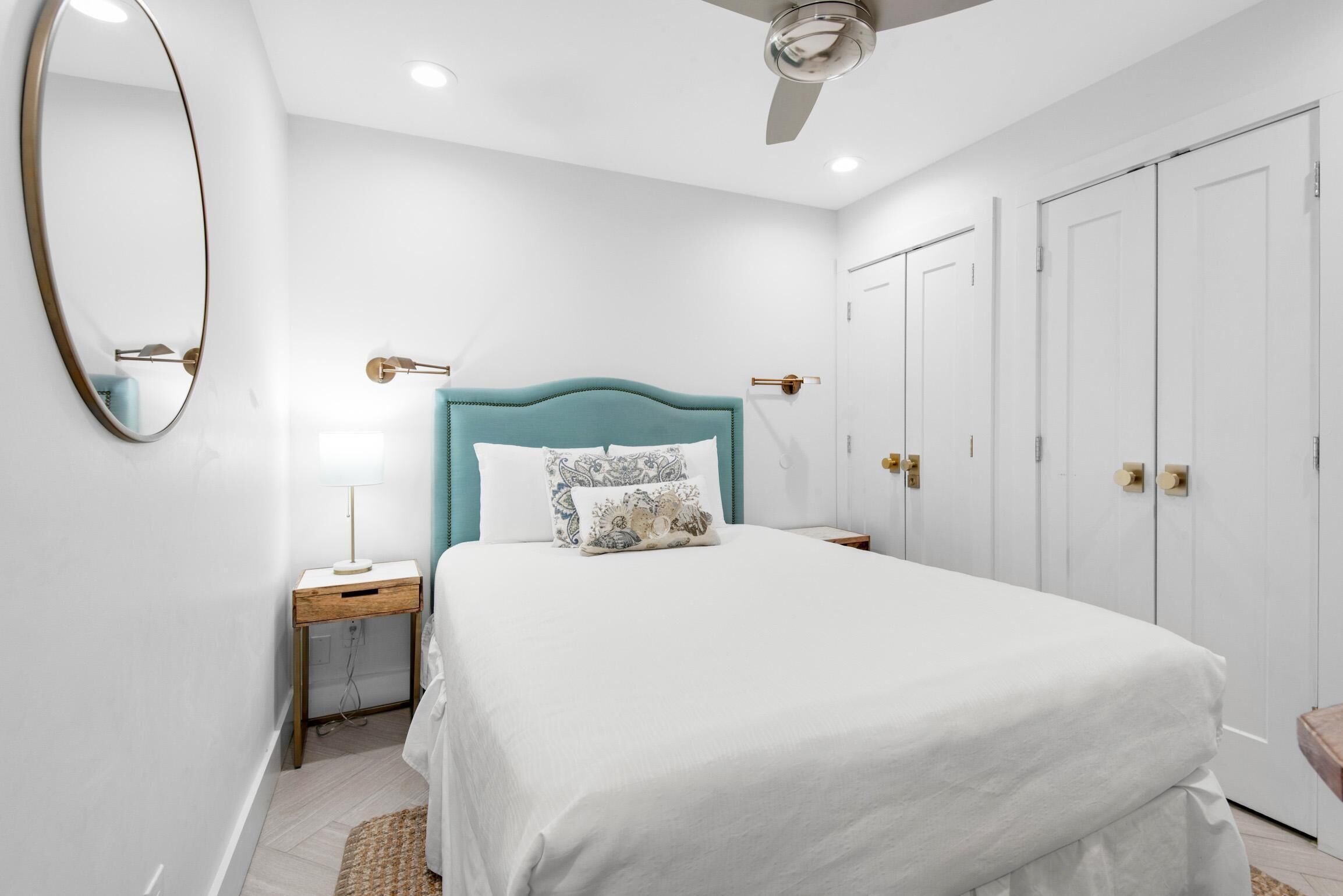 A bedroom with a bed, a nightstand, a mirror, a ceiling fan, and a wardrobe.