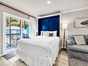 A hotel room with a bed, a gray sofa, a lamp, and a painting on the wall. - Inlet Sands 206- Inlet Dreams (Panama City Beach)