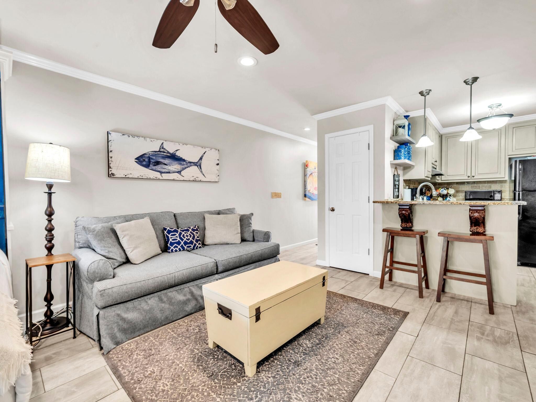 A living room with a grey sofa, a wooden coffee table, a lamp, and a painting of a fish on the wall.