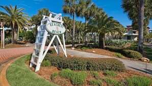 A sign for Seacrest Beach with a white structure and palm trees in the background. - Daze Gone Bye (Panama City Beach)