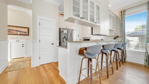 A kitchen with white cabinets, a stainless steel refrigerator, and a bar area with stools. - Daze Gone Bye (Panama City Beach)