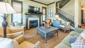 A cozy living room with a fireplace, comfortable seating, a flat-screen TV, and a staircase. - Comfort and Joy (Panama City Beach)