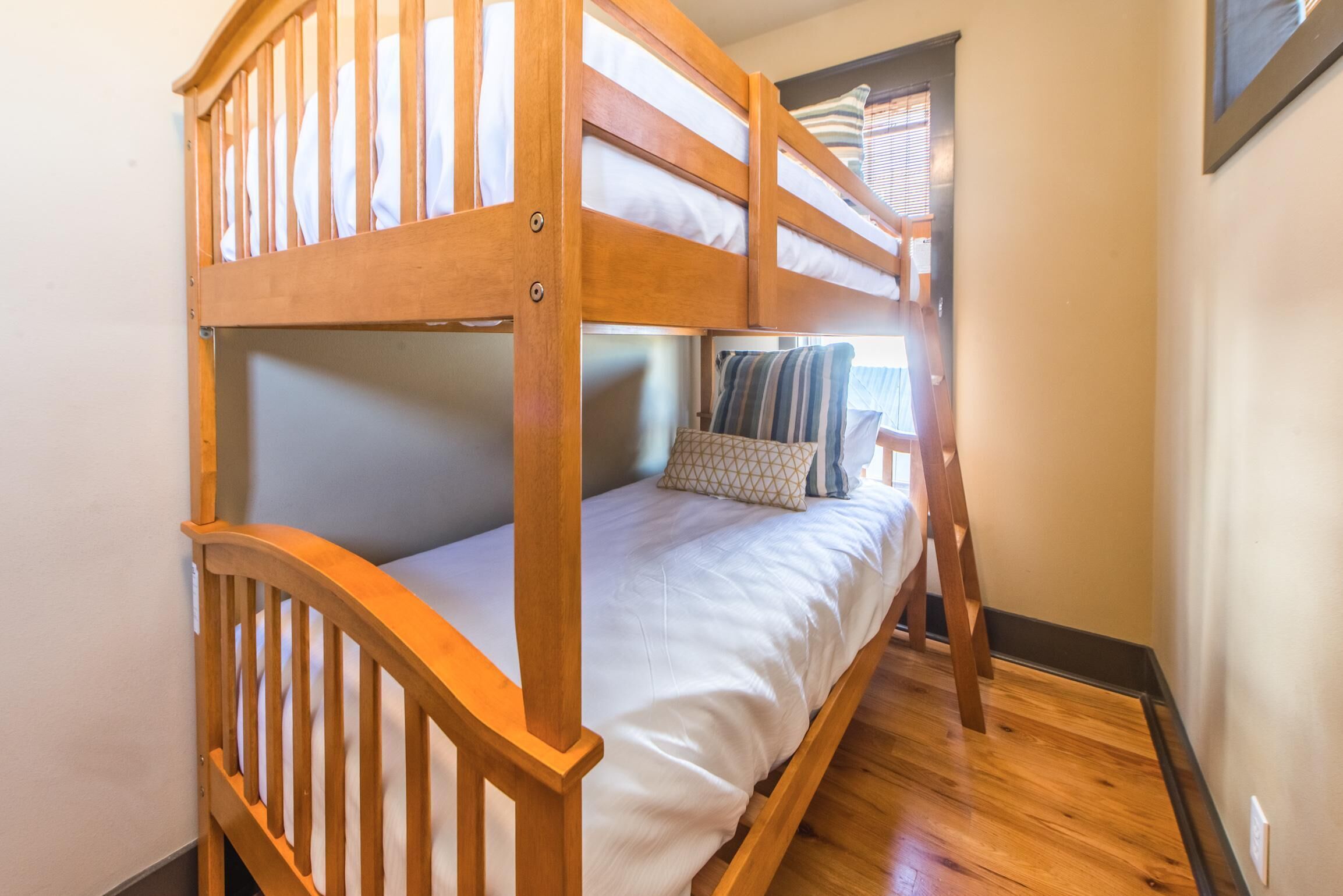 A bunk bed with a wooden frame, white bedding, and a small bedside table with a patterned pillow.