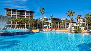 A large swimming pool with lounge chairs and palm trees, surrounded by hotel buildings. - Comfort and Joy (Panama City Beach)