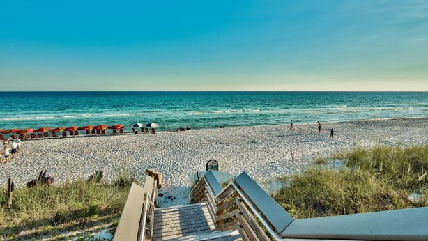 A beach with a wooden walkway leading to the water, umbrellas, and people. - Casa del Mar (Panama City Beach)