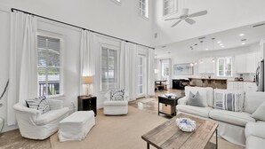 A spacious living room with a large sofa, a coffee table, and a dining area with a kitchen in the background. - Casa del Mar (Panama City Beach)