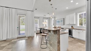 A modern kitchen with a central island, bar stools, pendant lighting, and a view of the outdoors. - Casa del Mar (Panama City Beach)