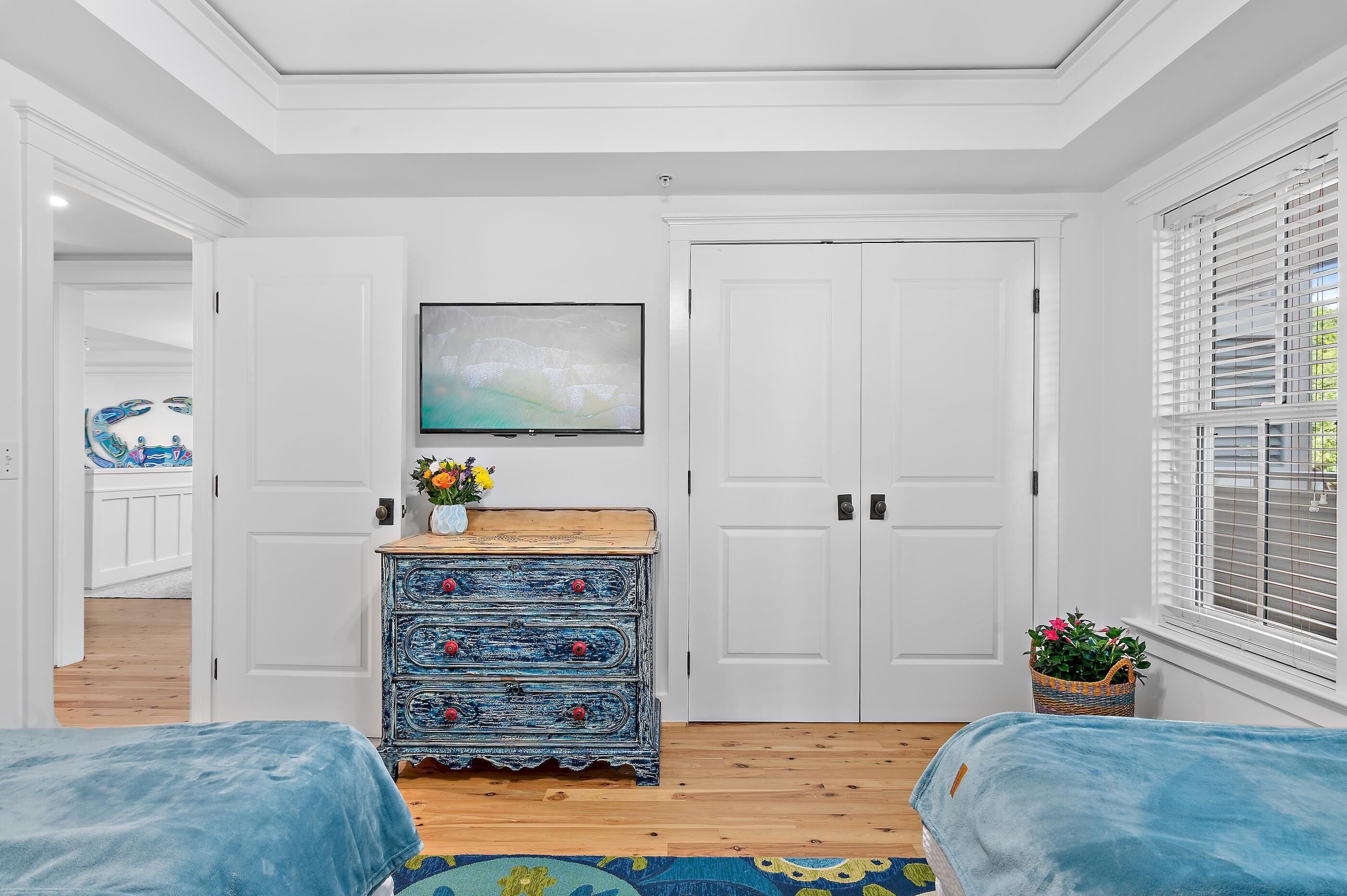 Un dormitorio con cama, cómoda, televisor y ventana con persianas.