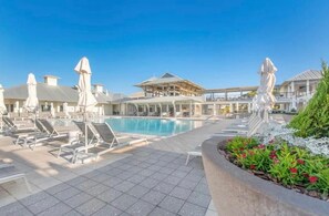 A pool area with lounge chairs and umbrellas, a covered seating area, and a building with a flat roof. - The Retreat 1848 (Santa Rosa Beach)