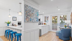 A modern kitchen with white cabinetry, blue bar stools, and a large abstract painting. - The Retreat 1848 (Santa Rosa Beach)