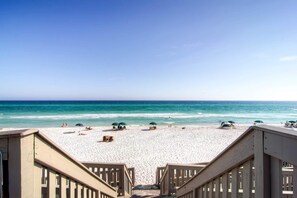 A beach view from a wooden deck with a staircase leading down to the sand.