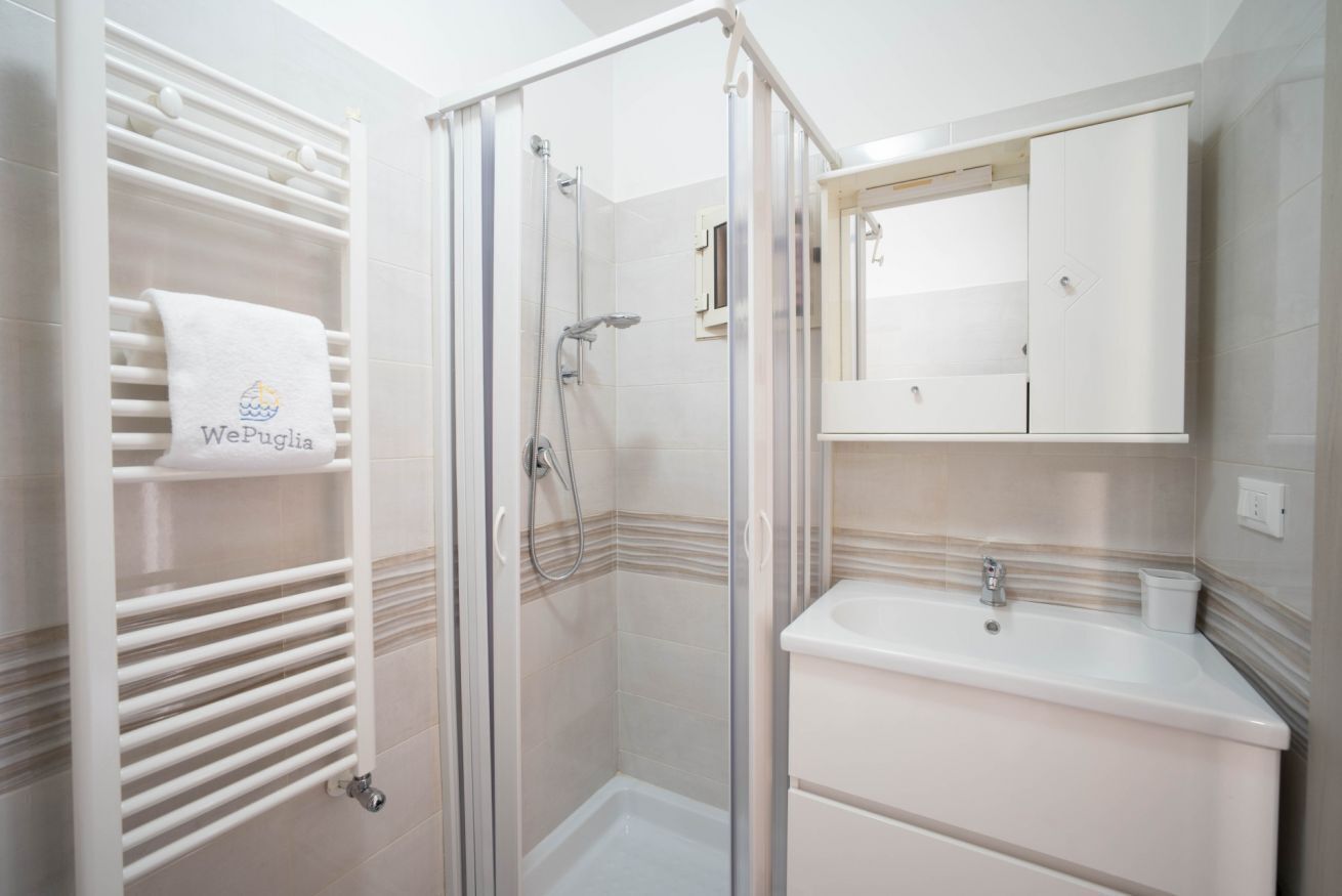 Un baño con cabina de ducha de vidrio, un lavamanos blanco y un perchero con una toalla.