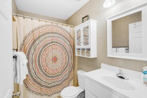 A bathroom with a patterned shower curtain, a white sink, and a cabinet with baskets. - Rollin Tide Villas- Rollin Tide B9 (Santa Rosa Beach)